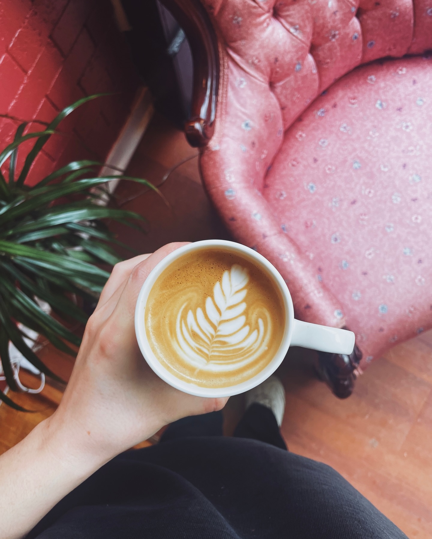 A hand holding latte art beside a vintage pink armchair